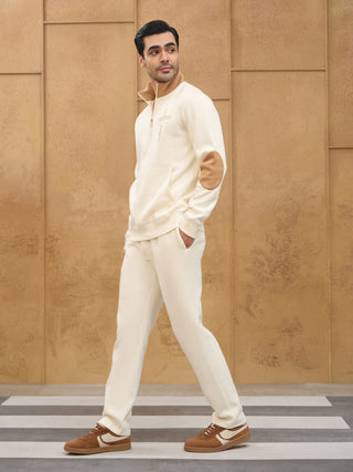 Men in a full shot, cream half-zip sweatshirt with tan accents and matching sweatpants, standing on a zebra crossing.