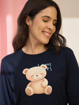 A woman poses in a navy blue long-sleeved pajama top with a cute teddy bear graphic and the text "I LOVE NAPS."