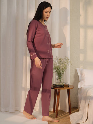 A woman poses in a plum-colored, long-sleeved pajama set with floral embroidery.