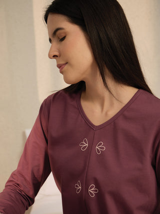 Women's long-sleeved V-neck top in plum with a subtle floral print, posed looking down.