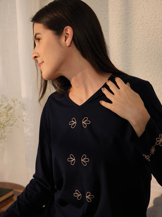 A woman in a navy blue v-neck pajama top with floral embroidery on the sleeves.