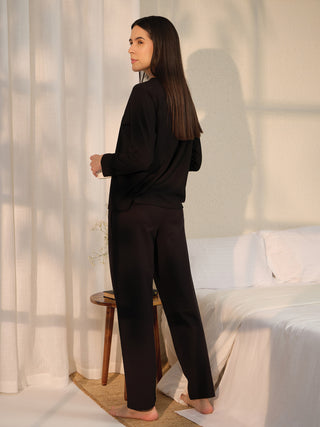 A woman stands in black sleepwear, holding a mug.