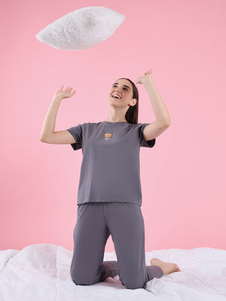 Woman in grey sleepwear with a bear print on the t-shirt, kneeling on a white bed and tossing a white fluffy pillow.