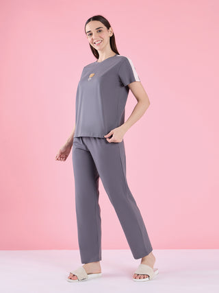 Woman in grey sleepwear with a bear print on the t-shirt, standing and posing against a pink background.