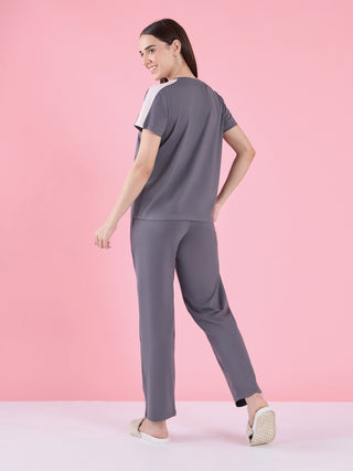 A woman in a grey t-shirt with white shoulder accents and matching grey pants, posing from the back.