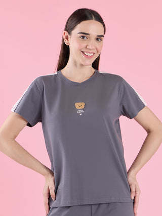 A woman in a grey t-shirt with white shoulder accents and matching grey pants, posing with her hands on her hips.