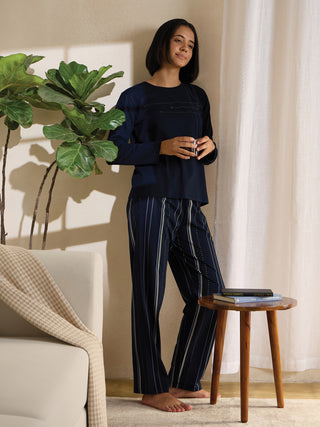 A woman stands and poses wearing navy blue striped sleepwear.