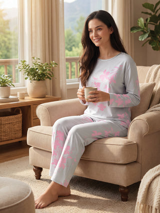 A woman wearing a light gray pajama set with pink floral print sits comfortably in a chair, holding a mug.