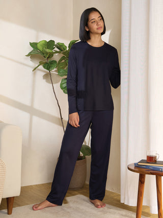 A woman wearing a navy blue long-sleeved top and matching pants with floral embroidery stands indoors.