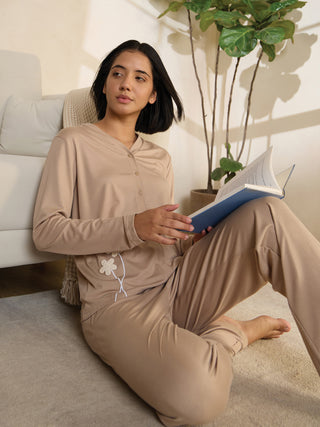 Women in beige printed sleepwear, sitting on the floor and reading a book.