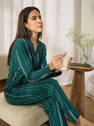 A woman in a teal striped pajama set holds a mug.