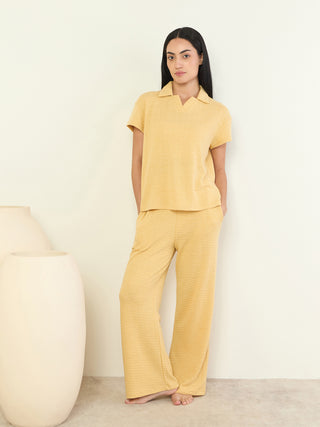 A woman poses in a yellow collared short-sleeve pajama top and matching wide-leg pants with a textured print.