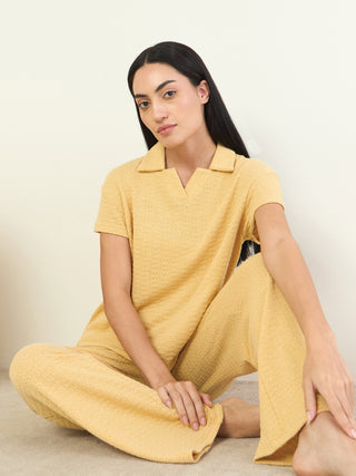 A woman poses in a yellow collared short-sleeve pajama top and matching wide-leg pants with a textured print.