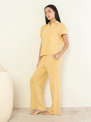 A woman models a yellow knit polo shirt and wide-leg pants, with a textured print, from a sleepwear company.