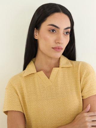 Women in a yellow, textured polo shirt with a V-neck and collar, arms crossed.