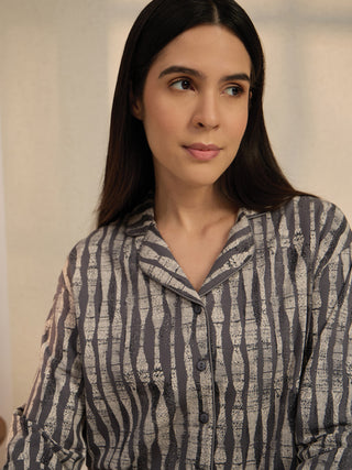 A woman in a grey and cream striped pajama set is looking off to the side.