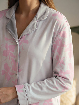 Women in a relaxed pose wearing a light purple long-sleeved pajama top with a pink floral print and grey velvet collar.