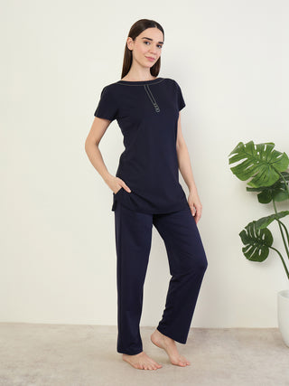 A woman poses in a navy blue pajama set, featuring a short-sleeved top with a boat neckline and button detailing.