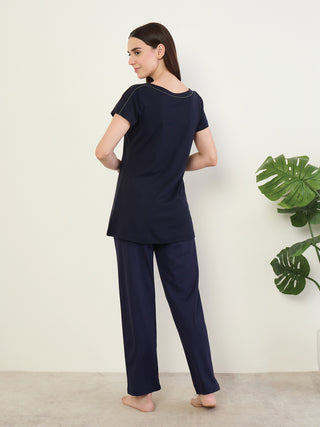 A woman poses in a navy blue pajama set, featuring a short-sleeved top with a boat neckline and decorative trim.