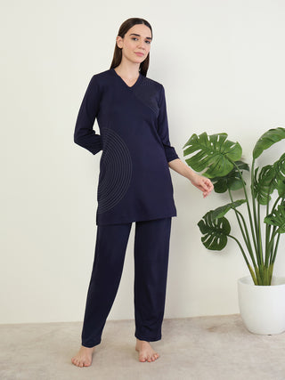 A woman stands wearing a navy blue long-sleeved top with subtle curved line detail and matching navy blue pants.
