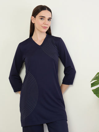 A woman stands with her hands in her pockets, wearing a navy blue V-neck tunic with a curved line print on the front and sleeves.