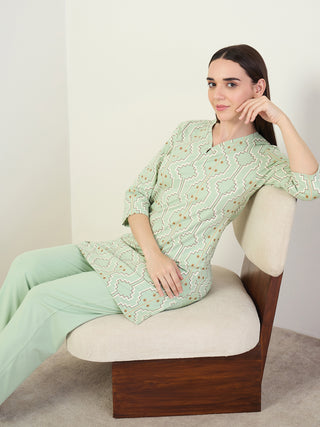 A woman is posing sitting in a chair wearing light green, printed sleepwear.