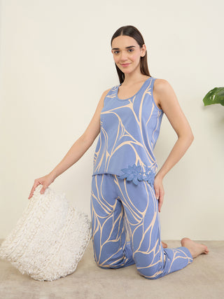 A woman kneels on the floor wearing blue and tan floral print pajamas, holding a white pillow.