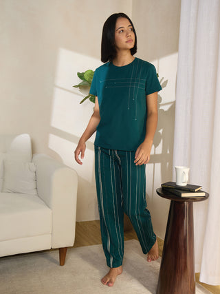 A woman in teal pajamas with a dotted line print walks past a couch and a side table.