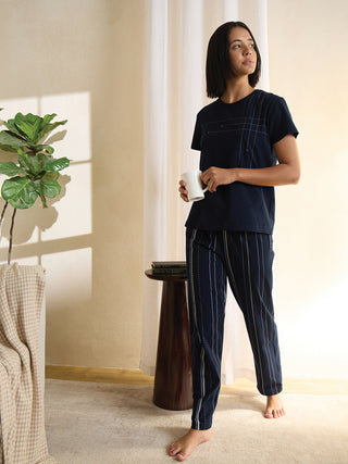 A woman in a navy blue pajama set with white dotted stripes and a stitched grid pattern on the top stands holding a mug.