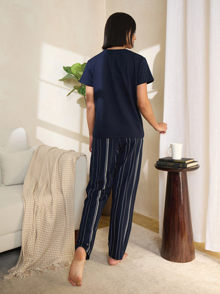 A woman in a navy blue pajama set with white vertical stripes stands facing away from the camera.