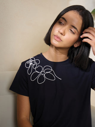 A woman in a navy blue t-shirt with embroidered white flowers poses playfully, with one hand touching her hair, as the other versions show her looking away and resting her head on her hand.