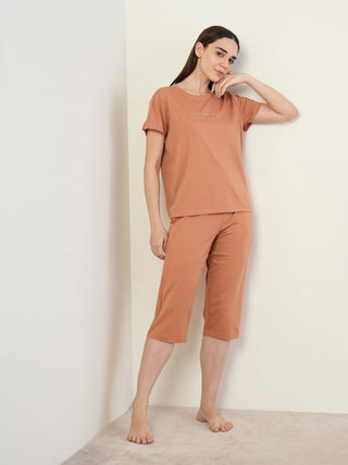 A woman stands leaning against a wall in a peach-colored pajama set with a simple print on the shirt.