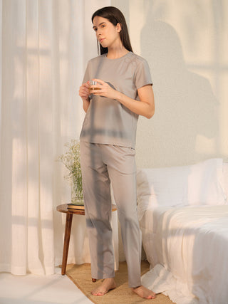 A woman in gray pajamas with a bow print stands holding a glass of amber liquid.