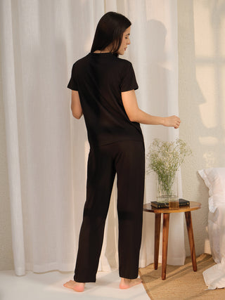 A woman in black pajamas stands with her back to the camera, looking over her shoulder.