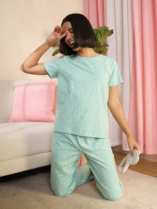 Women in a turquoise floral print pajama set, kneeling and holding a sleep mask.
