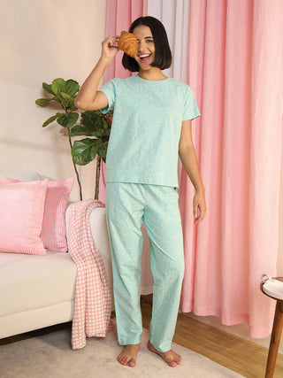 A woman in a light blue pajama set with a yellow floral print, holding a croissant to her eye.