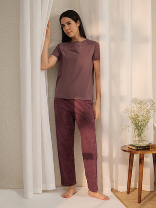 Women's maroon lace print pajama set, standing with hand on curtain.