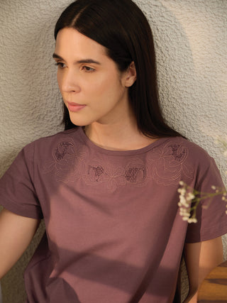 A woman wearing a mauve short-sleeved t-shirt with floral embroidery.