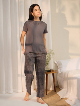 A woman stands in a dark grey pajama set with a floral print on the top and bottom, featuring a short-sleeved top and wide-leg pants, styled as part of a sleepwear collection.