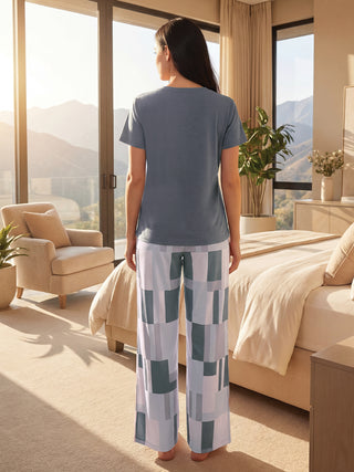 Women's grey short-sleeved pajama top with geometric print wide-leg pants, standing facing away from the camera in a bedroom.
