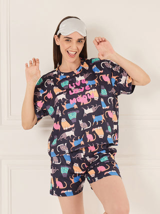 A woman in a dark blue t-shirt and shorts set featuring a playful cat print, striking a cheerful pose with her hands raised.