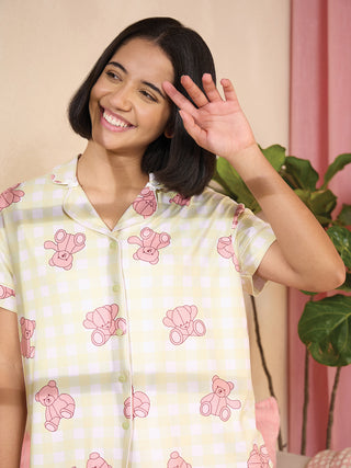 A woman in a pale yellow gingham pajama set with pink teddy bear print smiles and holds her hand up near her face.