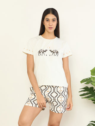 A woman in a white t-shirt with embroidered camels and patterned shorts poses for a sleepwear company.