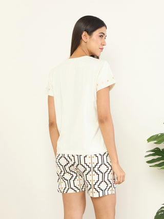 A woman is shown from the back, wearing a white t-shirt with gold accents on the sleeves and white shorts with a geometric black and gold print.