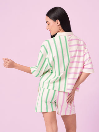 Women's cream pajama set with green and pink vertical stripes, shown from the back, with the model playfully extending her left arm.