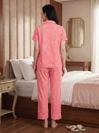 Women posing back to camera wearing coral pink printed pajamas, different from previous img due to the outfit's print.