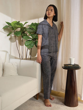 A woman poses wearing a short-sleeved, collared sleep shirt and pants set in grey with a black lace print.
