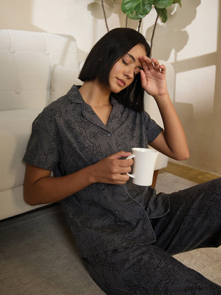 A woman in a gray floral print pajama set sits on the floor holding a mug.