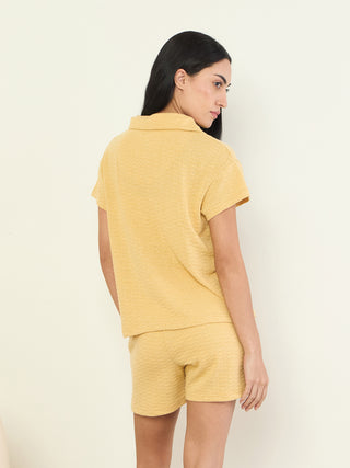 A woman models a yellow textured pajama set consisting of a short-sleeved collared top and shorts.