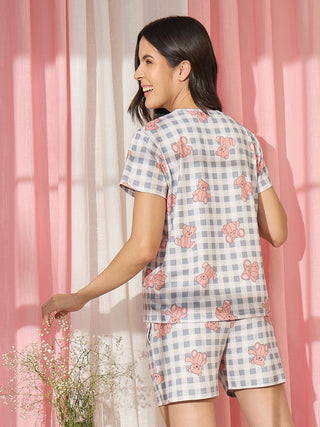 A woman in a gray and pink gingham pajama set with teddy bear prints, standing and touching flowers.